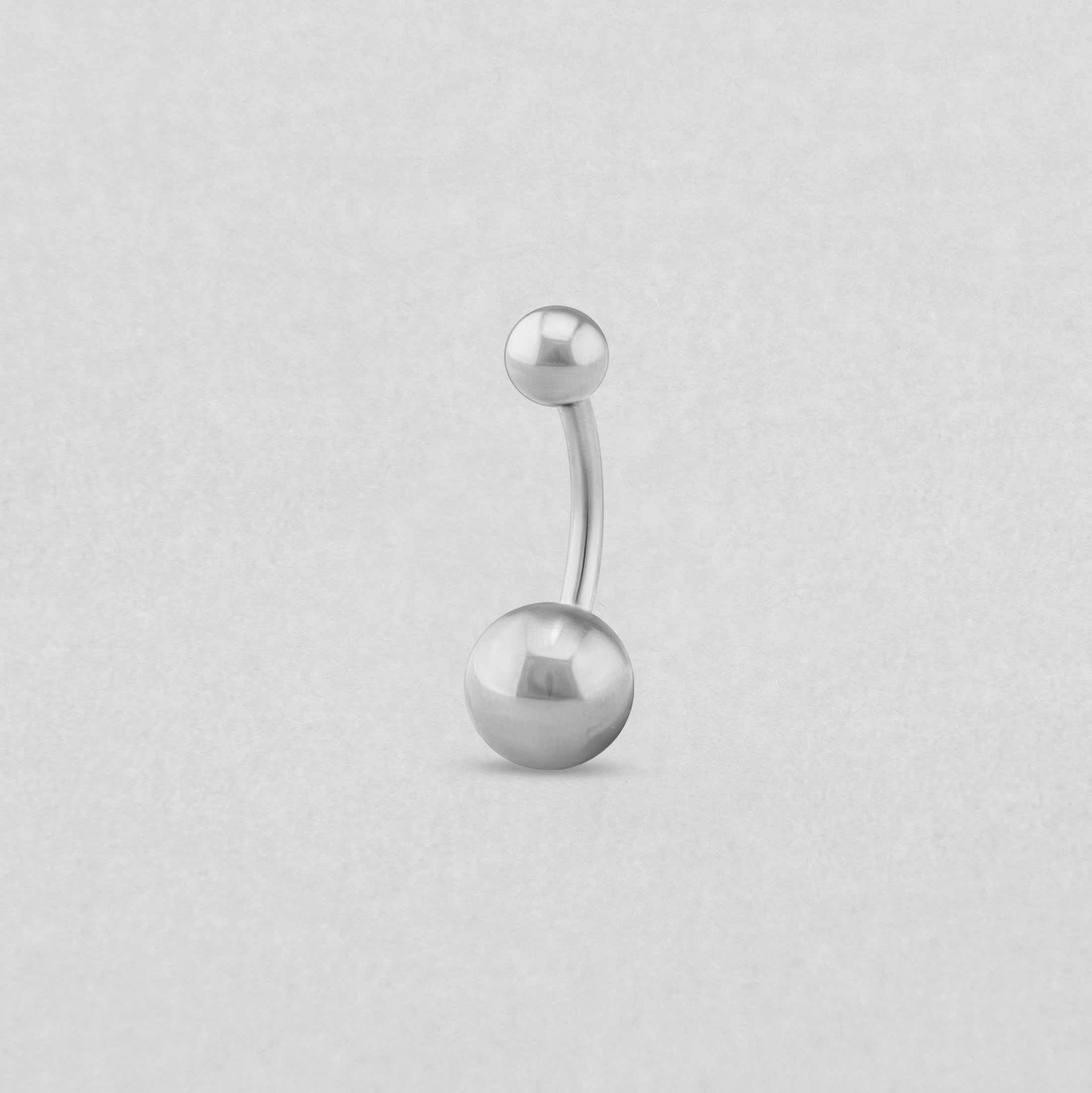 El piercing para el ombligo de NOBLE ART BEAUTY SOCIEDAD LIMITADA es una barra curvada de plata con extremos en forma de bola, uno pequeño y otro grande, ideal para cualquier colección de piercings, que se muestra sobre un fondo liso de color gris claro.
