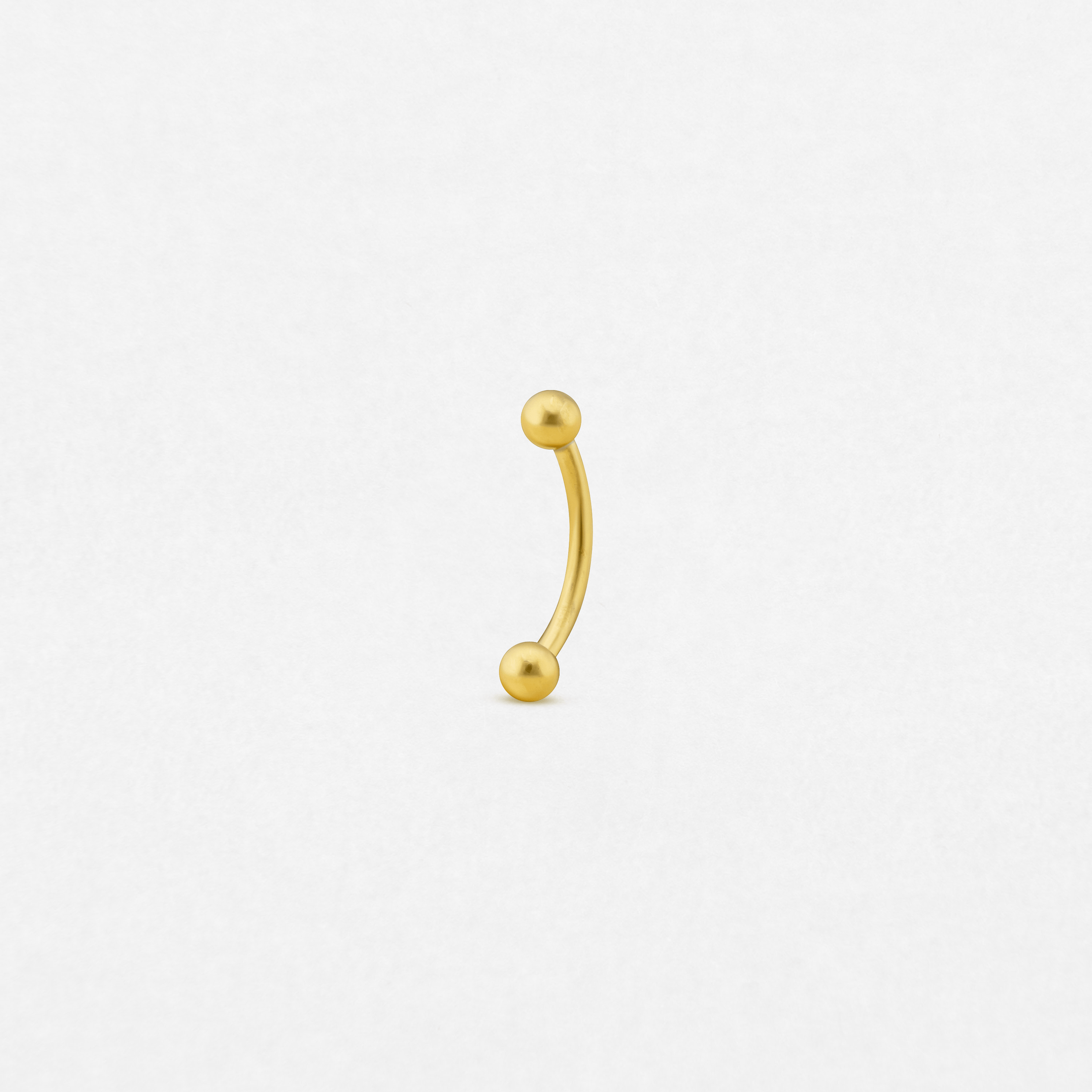 El «Banana» de NOBLE ART BEAUTY SOCIEDAD LIMITADA es un pequeño piercing tipo barra curvada de oro con extremos redondos en forma de bola, situado en el centro de un fondo blanco liso.