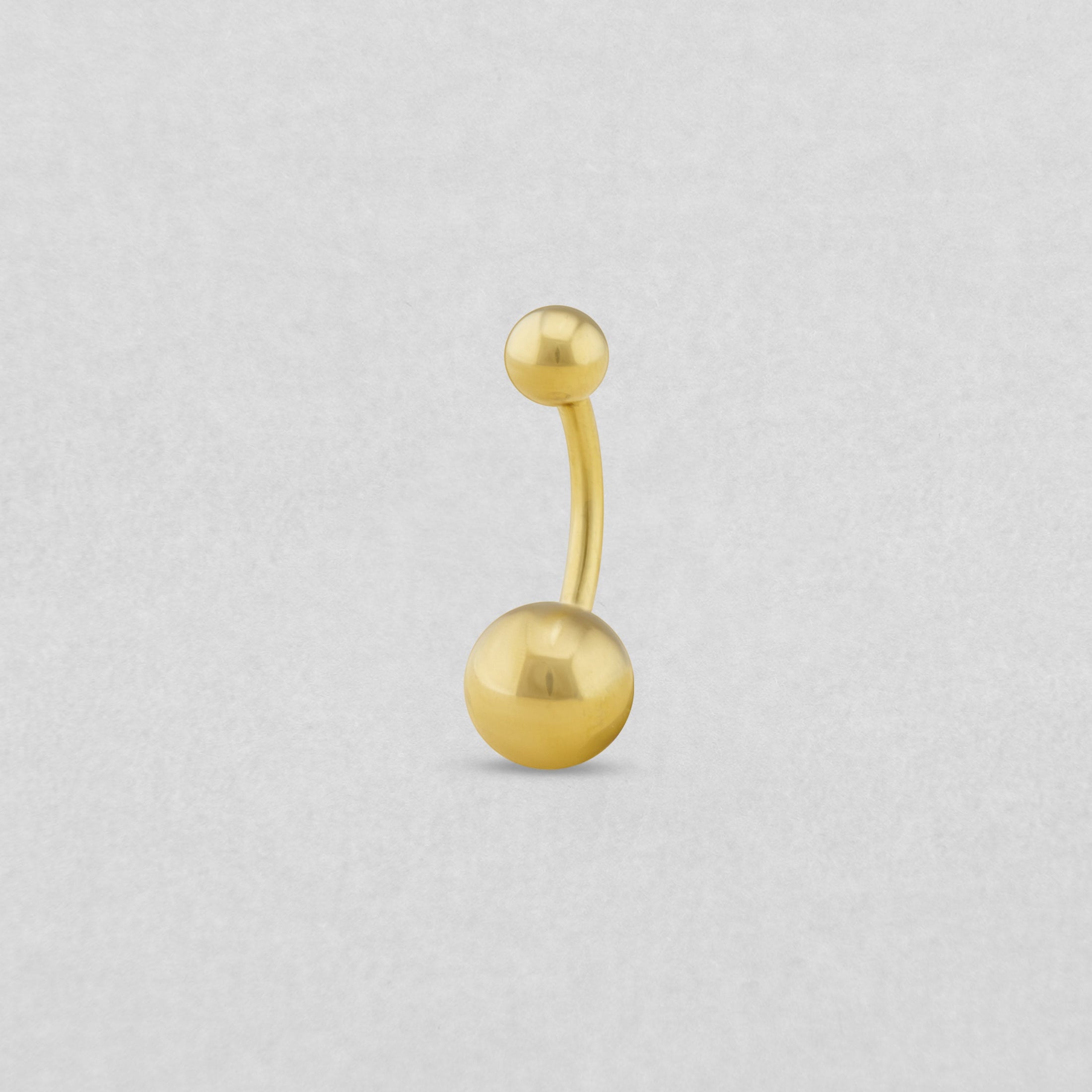 El piercing para el ombligo de NOBLE ART BEAUTY SOCIEDAD LIMITADA es un aro curvo dorado para el ombligo con una bolita en un extremo y otra más grande en el otro, que se muestra sobre un fondo gris claro. Perfecto para tu próximo piercing.